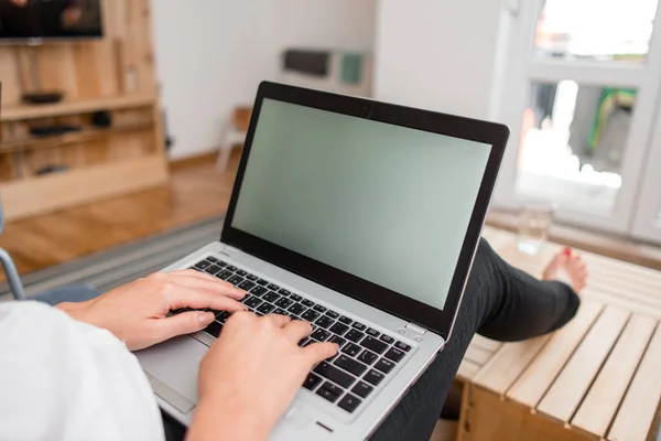 Юная леди, используя серый ноутбук и печатая черную клавиатуру обеими руками в комнате. Женщина в доме с офисными принадлежностями и технологическими устройствами . — стоковое фото