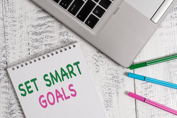 Написать текст Установить умные цели. Business concept for giving criteria to guide in the setting of objectives Top trendy metal laptop blank spiral notepad pens lying wooden table
.