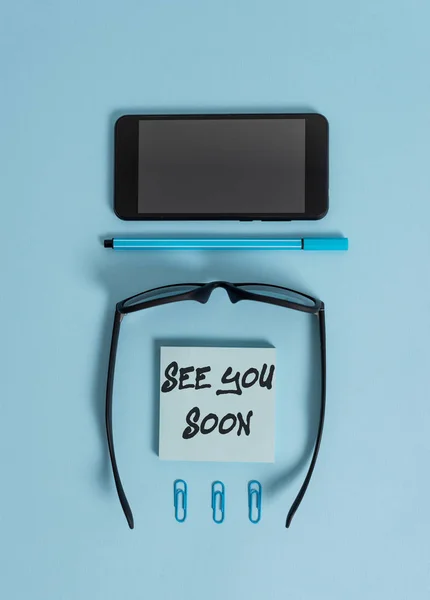 Writing note showing See You Soon. Business photo showcasing used for saying goodbye to someone and going to meet again soon Dark eyeglasses colored sticky note smartphone pen pastel background.