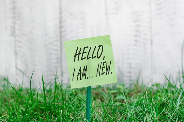 Word writing text Hello I Am New. Business concept for introducing oneself in a group as fresh worker or student Plain empty paper attached to a stick and placed in the green grassy land.