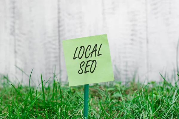 Word writing text Local Seo. Business concept for helps businesses promote products and services to local customers Plain empty paper attached to a stick and placed in the green grassy land. — Stock Photo, Image