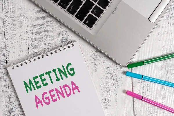 Word writing text Meeting Agenda. Business concept for items that participants hope to accomplish at a meeting Top trendy metallic laptop blank spiral notepad pens lying wooden table.