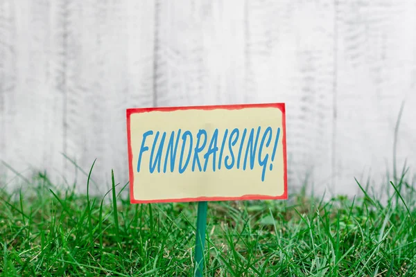 Writing note showing Fundraising. Business photo showcasing seeking to generate financial support for charity or cause Plain paper attached to stick and placed in the grassy land. — Stock Photo, Image