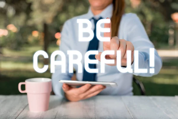 Signo de texto que muestra Ten cuidado. Foto conceptual asegurándose de evitar un posible percance de peligro o daño Mujer de negocios sentada junto a la mesa y sosteniendo el teléfono móvil . — Foto de Stock