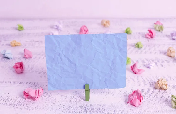 Pince à linge verte tenant un rectangle carré de papier de couleur dans un fond de bois blanc. Rappel de note froissé coloré dans un espace vide épinglé par un clip . — Photo