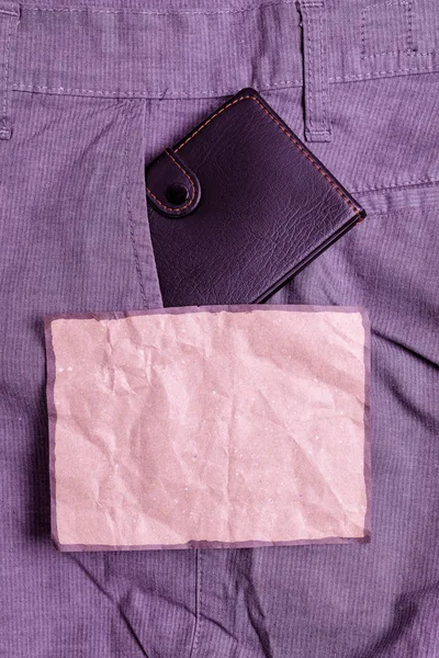 Liten plånbok i byxorna framficka bredvid brunt anteckningsblad. Lilla väskan är placerad inuti man Pants nära notationsark. Konstnärligt sätt att arrangera platt Lay Photography — Stockfoto