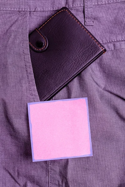 Liten plånbok i byxorna framficka bredvid rosa anteckningsblad. Lilla väskan är placerad inuti man Pants nära notationsark. Konstnärligt sätt att arrangera platt Lay Photography — Stockfoto