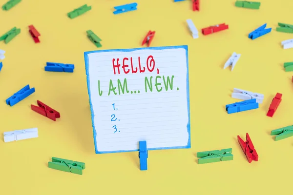 Handwriting text Hello I Am New. Concept meaning introducing oneself in a group as fresh worker or student Colored clothespin papers empty reminder yellow floor background office.