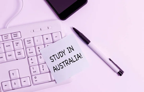 Handgeschreven tekst schrijven studie in Australië. Concept betekenis gaan in het buitenland orde Voltooi uw studies wit PC-toetsenbord met lege noot papier boven witte achtergrond. — Stockfoto