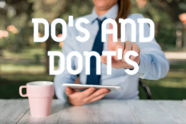 Señal de texto que muestra Do S And Dont S. Foto conceptual Reglas o costumbres relativas a alguna actividad o acciones Mujer de negocios sentada junto a la mesa y sosteniendo el teléfono móvil . —  Fotos de Stock