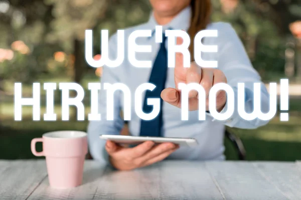Text sign showing We Re Hiring Now. Conceptual photo recently employ someone or pay someone to do particular job Female business person sitting by table and holding mobile phone. — Stock Photo, Image
