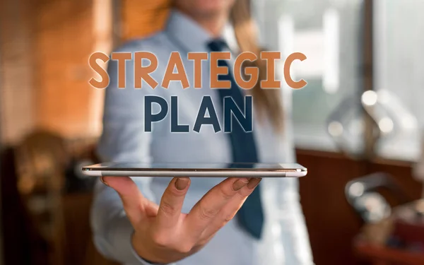 Writing note showing Strategic Plan. Business photo showcasing a systematic process of envisioning a desired future Blurred woman in the background pointing with finger in empty space. — Stock Photo, Image