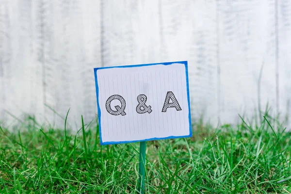手書きテキスト Q と質問。デモンストレーションが質問をし、別の人が棒に取り付けられ、緑の草原に置かれたプレーンな空の紙に答える概念の意味. — ストック写真