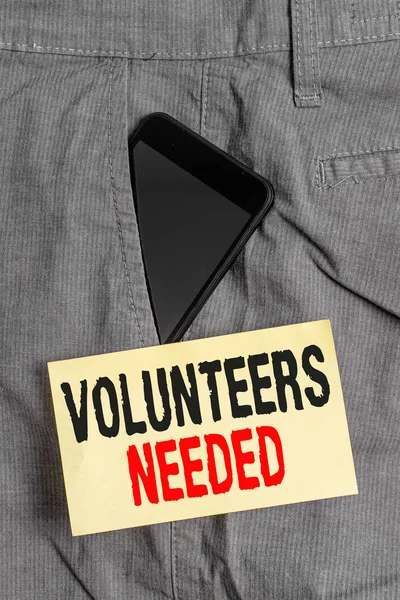Word writing text Volunteers Needed. Business concept for need work or help for organization without being paid Smartphone device inside formal work trousers front pocket near note paper.