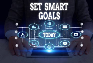 Akıllı Hedefler Kümesi'ni gösteren not yazma. İş fotoğraf vitrin hedefleri nin ayarında rehberlik etmek için kriterler veren Kadın akıllı cihaz kullanarak sunum sunan resmi iş elbisesi giymek.