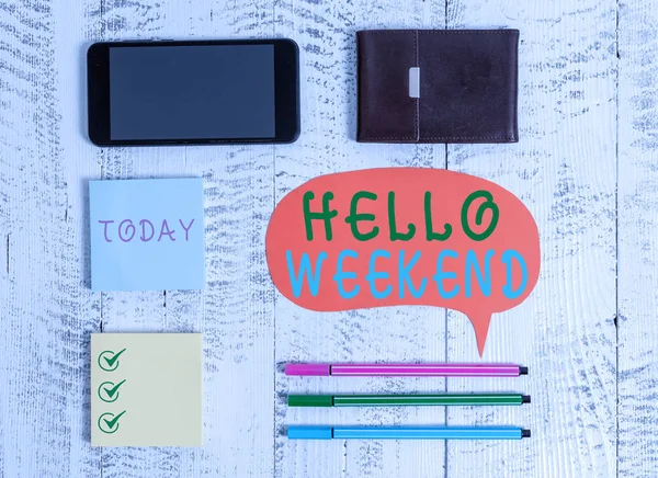 Word writing text Hello Weekend. Business concept for Getaway Adventure Friday Positivity Relaxation Invitation Smartphone pens blank speech bubble sticky notes wallet wooden background.