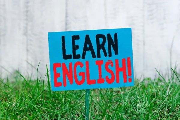 手写文本 学习英语。概念意义通过学习获得新语言知识 普通空纸附在棍子上，放在绿草丛中. — 图库照片