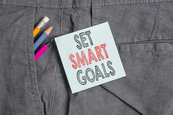 Handwriting text Set Smart Goals. Concept meaning giving criteria to guide in the setting of objectives Writing equipment and blue note paper inside pocket of man work trousers.