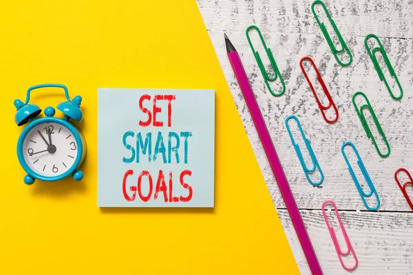 Handwriting text Set Smart Goals. Concept meaning giving criteria to guide in the setting of objectives Notepad marker pen colored paper sheet clips alarm clock wooden background.