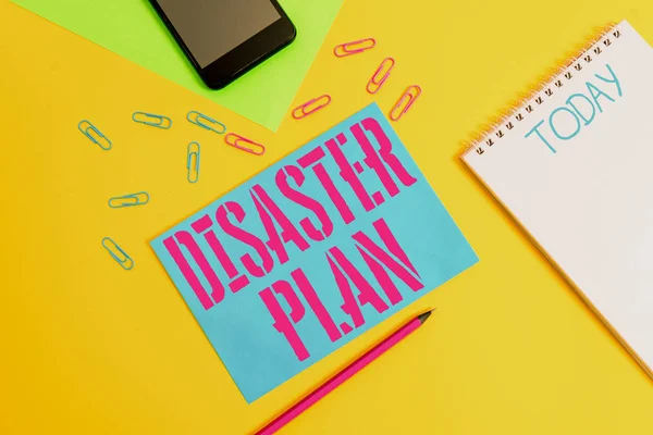 Word writing text Disaster Plan. Business concept for Respond to Emergency Preparedness Survival and First Aid Kit Blank spiral notepad pencil clips smartphone paper sheets color background.