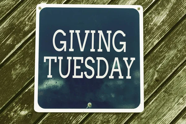 Handwriting text writing Giving Tuesday. Concept meaning international day of charitable giving Hashtag activism Empty blue board with copy space above wooden background.