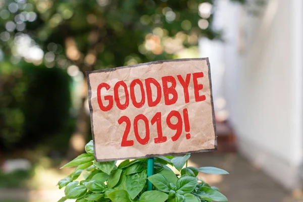 Writing note showing Goodbye 2019. Business photo showcasing express good wishes when parting or at the end of last year Plain paper attached to stick and placed in the grassy land.