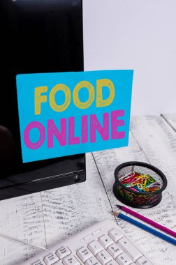 Food Online'ı gösteren bir not yazıyorum. Klavye nin yakınındaki siyah bilgisayar ekranına bantlanmış telefon uygulaması veya web sitesi Kullanarak yemek yiyecek bir şeyler isteyen iş fotoğrafı.