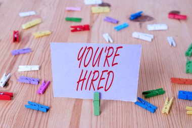 El yazısı metin You Re Hired. Kavram anlamı Yeni İş İstihdam Newbie Kayıtlı Kabul İşe Renkli clothespin kağıtları boş hatırlatma ahşap zemin arka plan ofis.