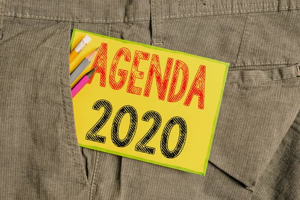 Handwriting text writing Agenda 2020. Concept meaning list of activities in order which they are to be taken up Writing equipment and yellow note paper inside pocket of man work trousers.