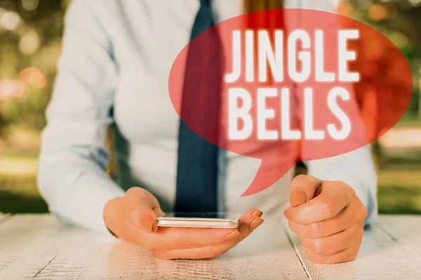 Γράφω σημείωμα που δείχνει τρίγωνα κουδούνια. Επιχειρηματική φωτογραφία παρουσιάζοντας το πιο διάσημο παραδοσιακό χριστουγεννιάτικο τραγούδι σε όλο τον κόσμο γυναικεία επιχείρηση που κάθεται δίπλα στο τραπέζι και κρατώντας κινητό τηλέφωνο. — Φωτογραφία Αρχείου
