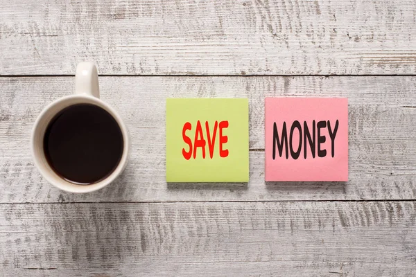 Escritura de texto a mano Ahorre dinero. Concepto que significa almacenar un poco de su dinero cada mes para usarlos en algún momento más tarde estacionario colocado junto a una taza de café negro sobre la mesa de madera . —  Fotos de Stock