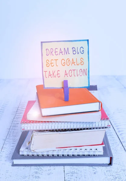 Word writing text Dream Big Set Goals Take Action. Business concept for Motivation to follow your dreams Inspiration pile stacked books notebook pin clothespin colored reminder white wooden.