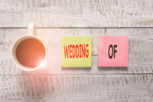 Handwriting text writing Wedding Of. Concept meaning announcing that analysis and woanalysis now as married couple forever Stationary placed next to a cup of black coffee above the wooden table.