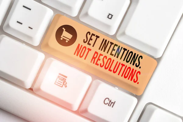 Text sign showing Set Intentions Not Resolutions. Conceptual photo Positive choices for new start achieve goals White pc keyboard with empty note paper above white background key copy space.