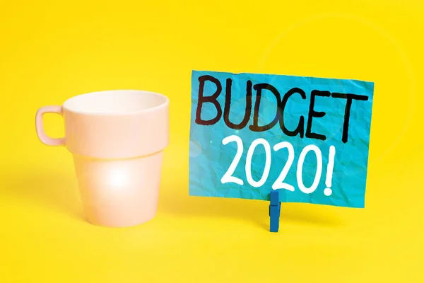 Handwriting text Budget 2020. Concept meaning estimate of income and expenditure for next or current year Cup empty paper blue clothespin rectangle shaped reminder yellow office.