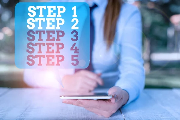 Nota de redação mostrando os passos 1, 2, 3, 4 e 5. Foto de negócios mostrando os níveis de um processo de fluxo de trabalho Feminino empresário sentado à mesa e segurando o telefone móvel . — Fotografia de Stock