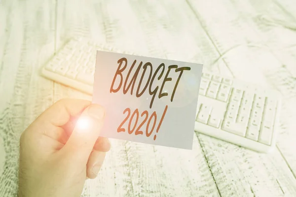 Text sign showing Budget 2020. Conceptual photo estimate of income and expenditure for next or current year man holding colorful reminder square shaped paper white keyboard wood floor.