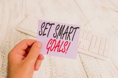 Akıllı Hedefler Kümesi'ni gösteren metin işareti. Kavramsal fotoğraf listesi fikirodak çabaları açıklığa kavuşturmak için renkli hatırlatma kare kağıt beyaz klavye ahşap zemin tutan zaman akıllıca adam kullanın.