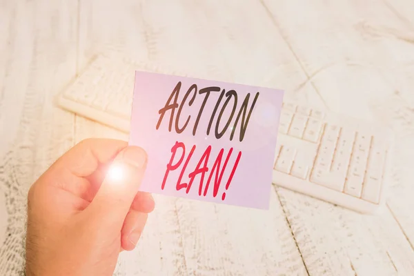 Text sign showing Action Plan. Conceptual photo proposed strategy or course of actions for certain time man holding colorful reminder square shaped paper white keyboard wood floor.