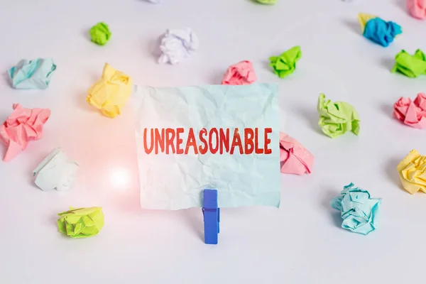 Handwriting text Unreasonable. Concept meaning Beyond the limits of acceptability or fairness Inappropriate Colored crumpled papers empty reminder white floor background clothespin. — Stockfoto