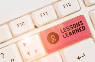 Ders Öğrenilmiş 'i gösteren bir not yazıyorum. Deneyimle elde edilen bilgi veya anlayışı gösteren iş fotoğrafı beyaz arkaplanın üzerinde nota kağıdıyla birlikte beyaz pc klavye.