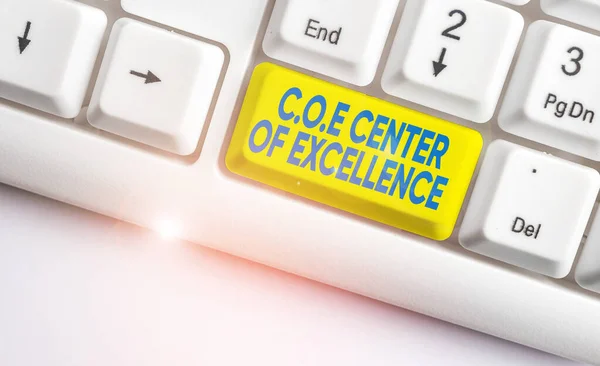 Handwriting text writing Coe Center Of Excellence. Concept meaning being alpha leader in your position Achieve White pc keyboard with empty note paper above white background key copy space.