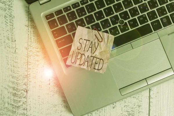 Text sign showing Stay Updated. Conceptual photo keep modern recent or containing the latest information Trendy metallic laptop crushed colored paper note lying old wooden table.