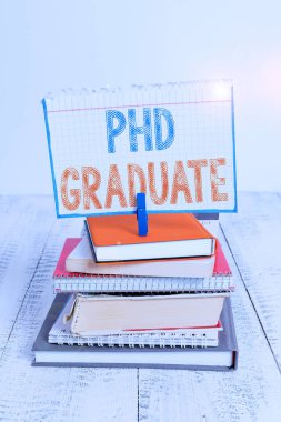 Doktora derecesini gösteren bir mesaj. Bir kurs yığınından sonra verilen kavramsal fotoğraf en yüksek üniversite diploması. Kitaplar dizilmiş, çamaşır mandalı renkli hatırlatıcı beyaz ahşap..