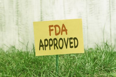 Fda 'nın onaylandığını gösteren bir not yazıyorum. Fda, ürünün ya da formülün güvenli ya da etkili olduğunu kabul etti. Çimenli topraklara yapıştırılmış sade kağıt..