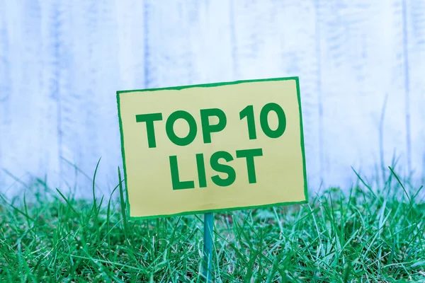 Χειρόγραφο κείμενο γραφής Top 10 List. Έννοια που σημαίνει τα δέκα πιο σημαντικά ή επιτυχημένα στοιχεία σε μια συγκεκριμένη λίστα Απλό άδειο χαρτί που συνδέεται με ένα ραβδί και τοποθετείται στην πράσινη χλοώδη γη. — Φωτογραφία Αρχείου