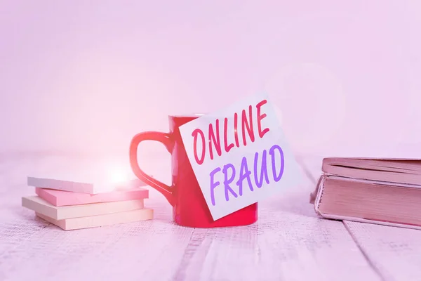 Text sign showing Online Fraud. Conceptual photo use of Internet services to deceive victims and steal money Coffee cup blank sticky note stacked note pads books retro old wooden table.