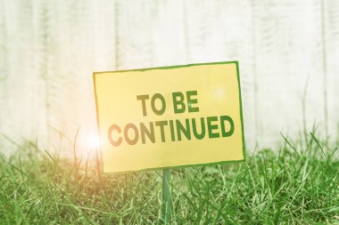 Devam Etmek için el yazısı metni. Kavram anlamı, hikayenin bir sonraki bölümde devam ettiğini gösteriyor. Bir sopaya bağlanmış boş kağıt yeşil çimenli topraklara yerleştirilmiş..