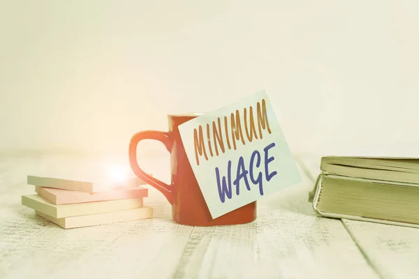 Text sign showing Minimum Wage. Conceptual photo the lowest wage permitted by law or by a special agreement Coffee cup blank sticky note stacked note pads books retro old wooden table.