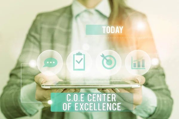 Writing note showing Coe Center Of Excellence. Business photo showcasing being alpha leader in your position Achieve Female human wear formal work suit presenting smart device.